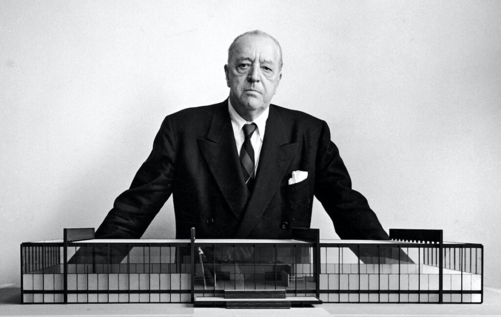 Ludwig Mies van der Rohe, architecte, pris en photo devant une maquette.